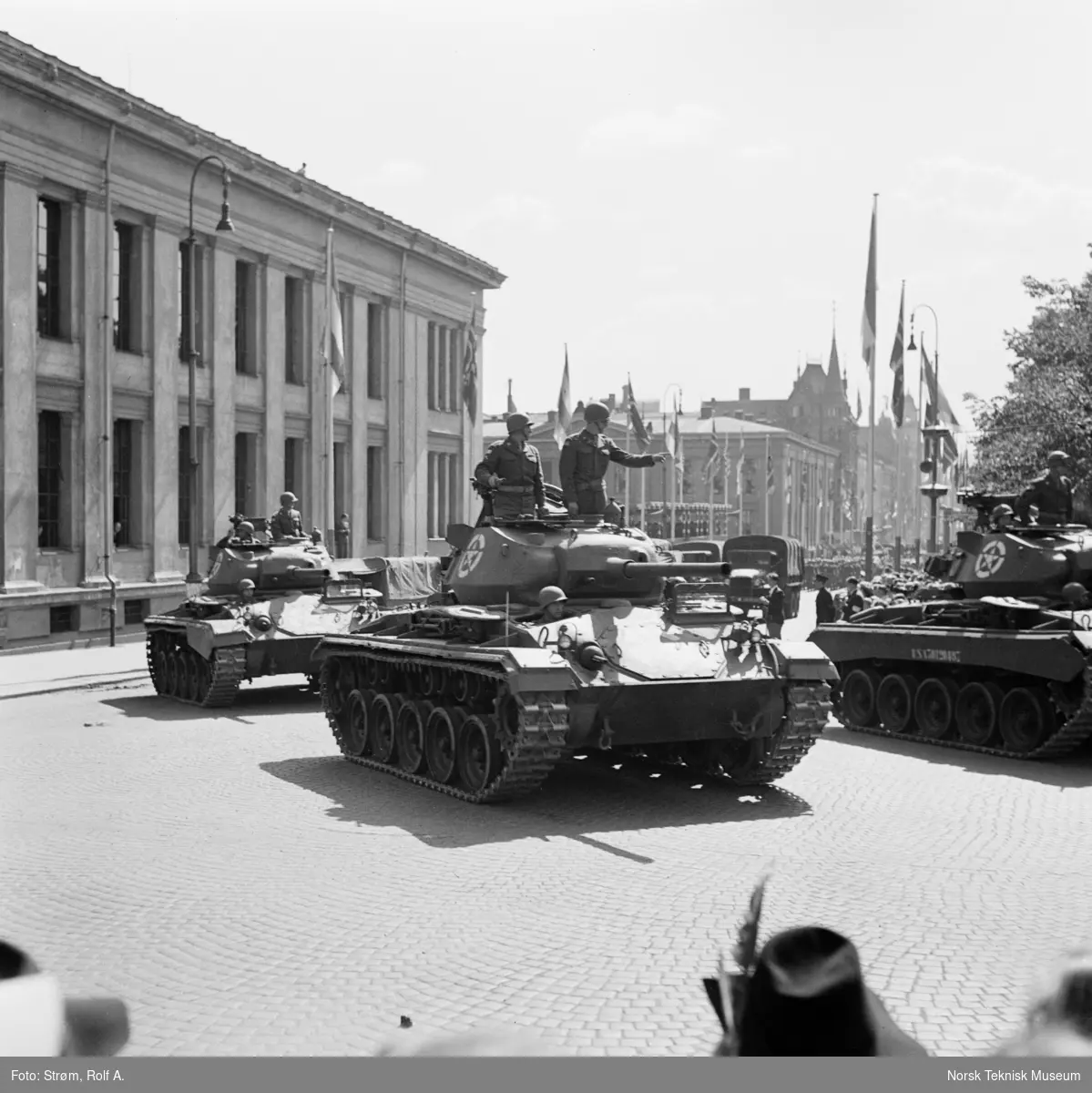 Opptog, USAs nasjonaldag, tanks med stående soldater passerer tilskuere ved Universitetet, gata er pyntet med norske, amerikanske og andre nasjonaliteters flagg, Oslo, 4. juli 1945.