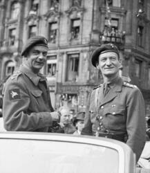 To menn i militære uniformer på en bil, foran folkemengde, O
