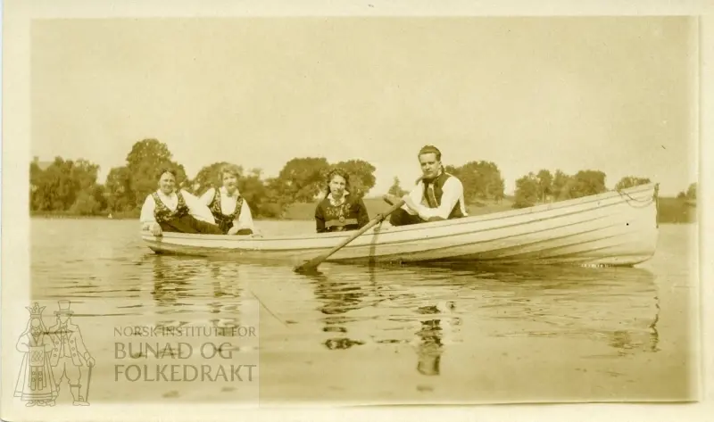 3 kvinner og en mann i bunad - i en robåt.