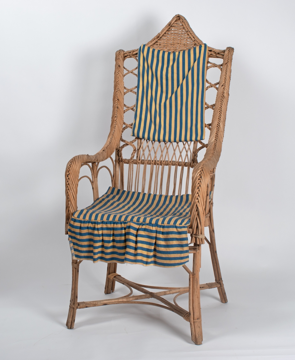 Kurvstol med høy rygg og armlener. Stolen har lett og åpen konstruksjon. Dekorative elementer med ulike typer fletting. Stolen har løs setepute og en liten, løs ryggpute.