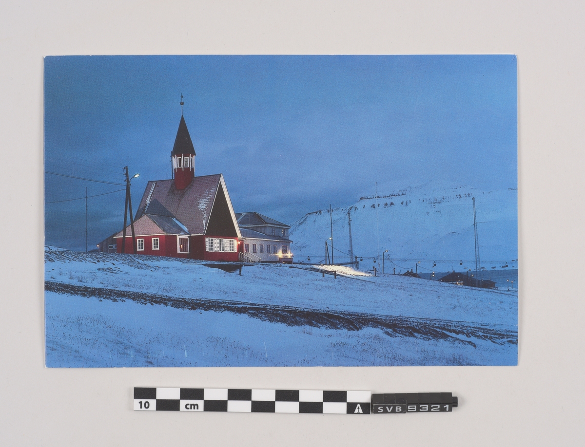 Dobbeltsidig kort. Fotografi av kirken i Longyearbyen på fremsiden. Håndskrevet hilsen og stempel på innsidens høyre side. Trykk på baksiden. Hull i hjørnet av kortet.