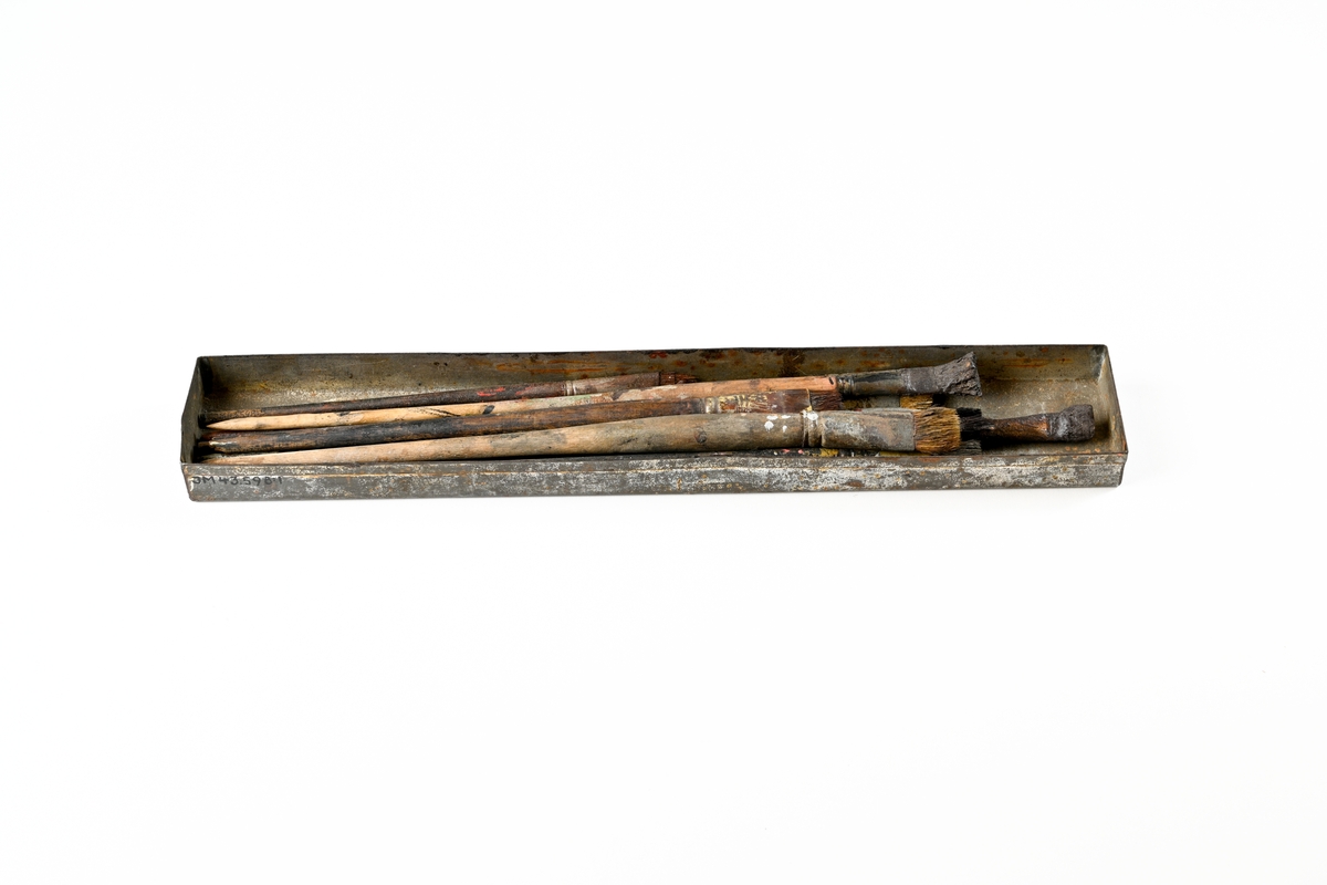 Målarskrin av bleckplåt, avlångt, öppet skrin med 11 penslar av trä och borst. Penslarna är använda och har färgrester kvar.