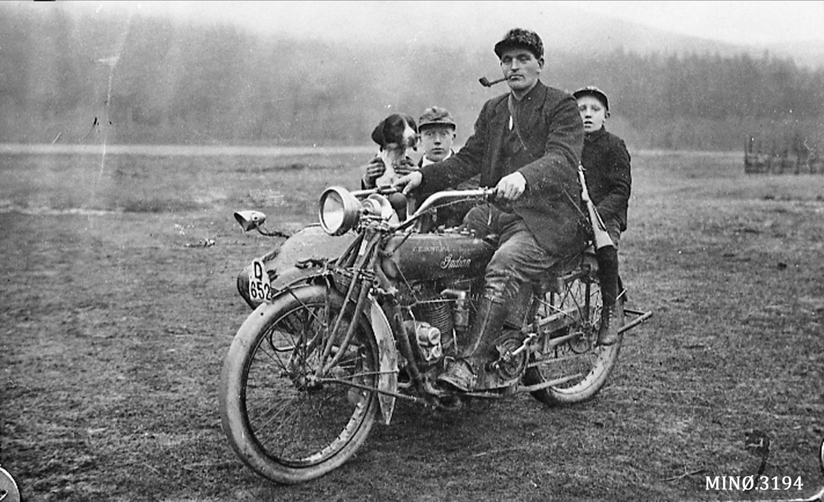 Mann sittende på motorsykkel med sidevogn, unge bakpå, pers i sv. 