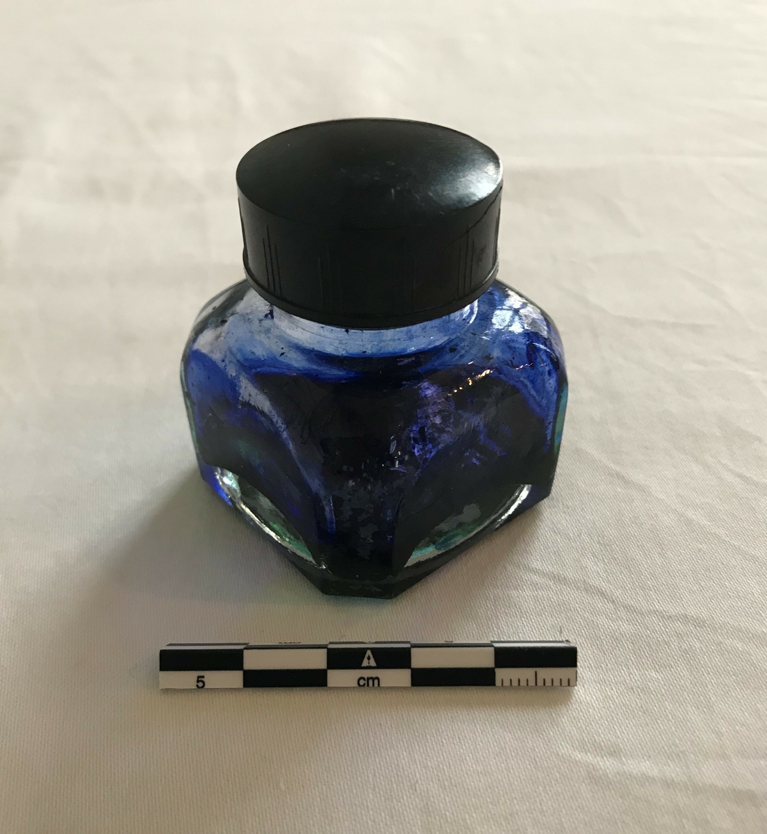 Åttekantet glasflaske med skrukork. Rester av blått blekk i flasken. 