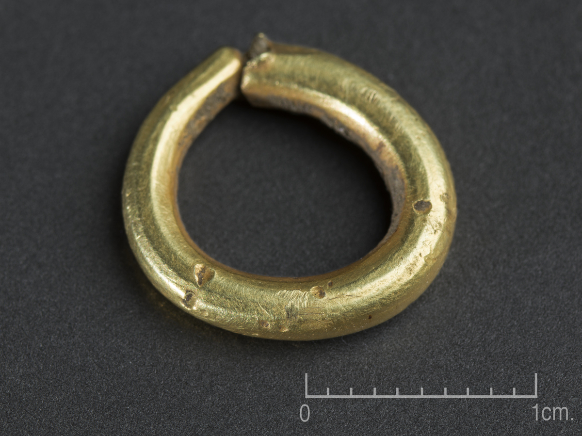 Betalingsring av gull i en vinding, ytre diam. 15 mm og indre diam. 10 mm. Ringen er mellom 2-3 mm tykk og øker i tykkelse fra en ende. Den tykkeste enden er markert avknekt med en fasett inn mot bruddflaten på yttersiden av ringen.