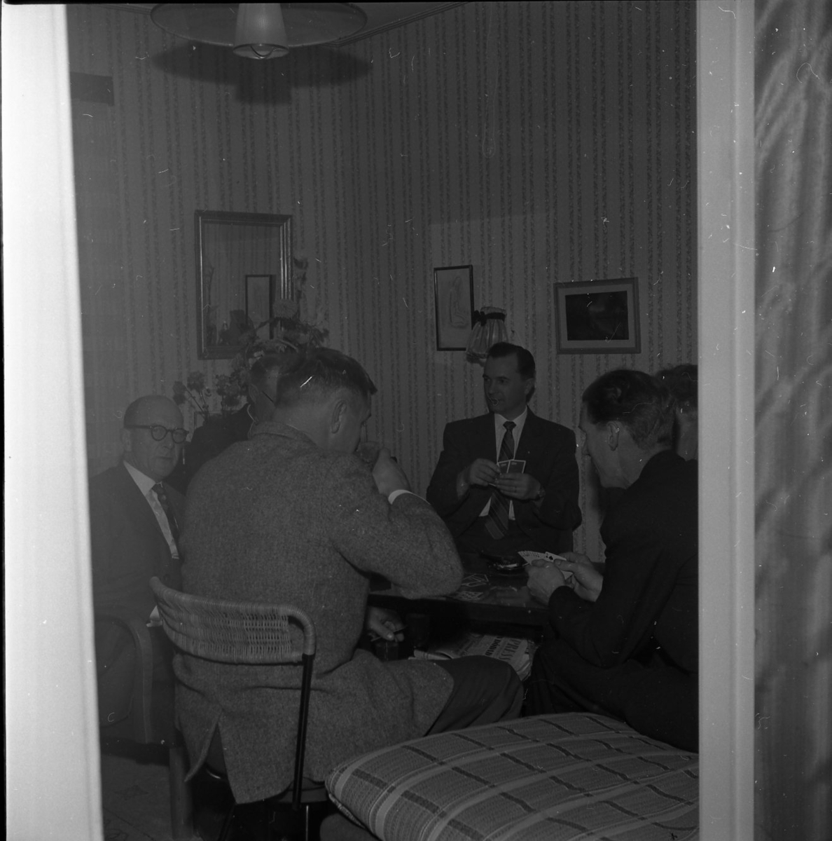 Sex män sitter runt ett bord och spelar kort.