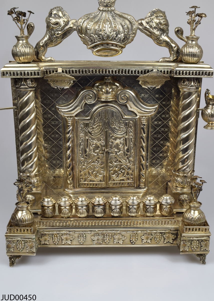 Chanukaljusstake tillverkad av silver med oljehållare, blomsterdekor och krona flankerad av lejon.
