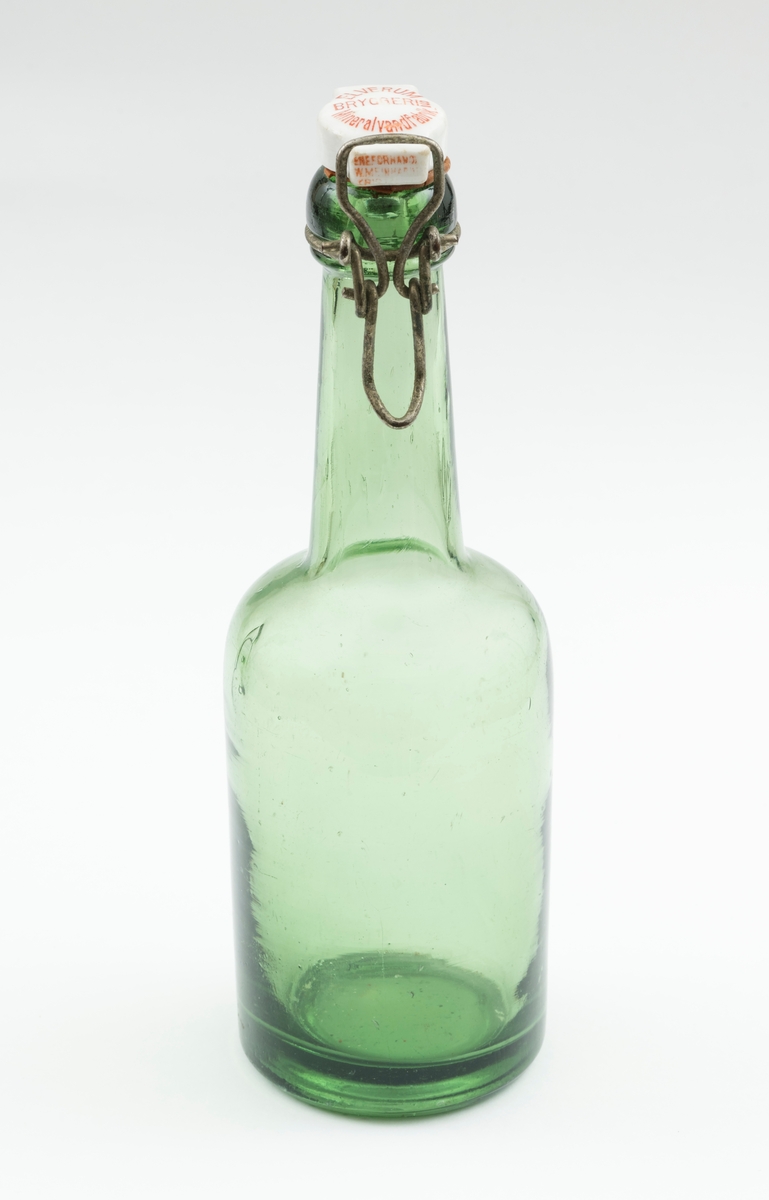 Flaske av grønt glass, antakelig opprinnelig brus- eller ølflaske, som kan ha vært gjenbrukt til aldre drikkevarer, for eksempel husholdningssaft. Flaska er 20,0 centimeter høy (uten kork). Den har en sylindrisk kropp med cirka 6,9 centimeters diameter. Cirka 10 centimeter fra standflata går den sylindriske delen over i ei innoverskrånende skulder mot en mer sylindrisk hals. Den midtre delen av flaskebotnen er oppoverkuvet. Flaska kan romme cirka 3 desiliter væske. Godset omkring munningen - «flasketuten» - er noe tjukkere enn i flaska for øvrig, og her er det et spor som har gitt feste for en såkalt «patentkork». Dette er en propp, utført i kvitt porselen, som er hengslet til flasketuten ved hjelp av ståltråd, som er forankret i det nevnte sporet omkring flasketuten slik at proppen faller ned i flaskemunningen og kan låses der ved hjelp av ei ståltrådspenne, som når flaska lukkes omslutter en tapp i den fremre enden av porselenselementet. Undersida av denne komponenten har vært utstyrt med en rødfarget gummipakning, som skulle skape et vakuum i flaska. Her er pakningen bare delvis intakt. Oversida av porselenselementet er merket «ELVERUM BRYGGERIs Mineralvandfabrik» (jfr. fotografiet SJF-F.013394).
