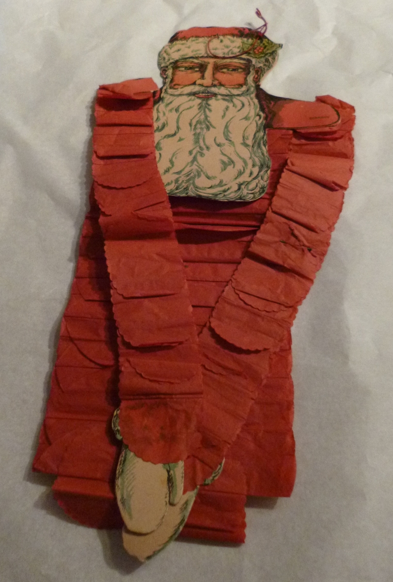 Julenissefigur.  Kroppen består av krepp-papir mens ansikt og hender er i papp.
