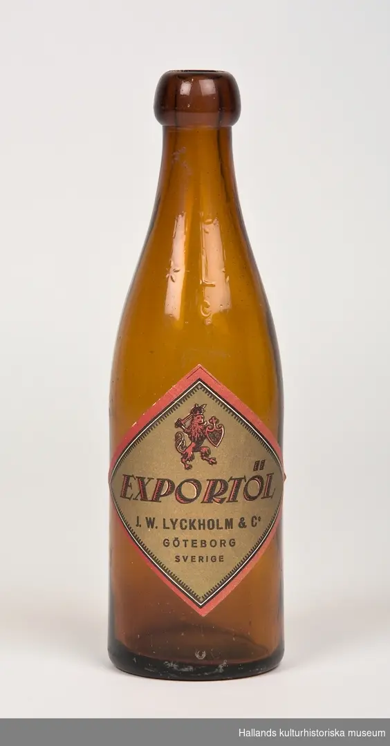Ölflaska. Flaskan är tillverkad av brunt klarglas och har en pappersetikett med texten: "Exportöl J.W. Lyckholm & co Göteborg Sverige". 33cl.

I glaset finns följande text graverat: "* L *" och "C"