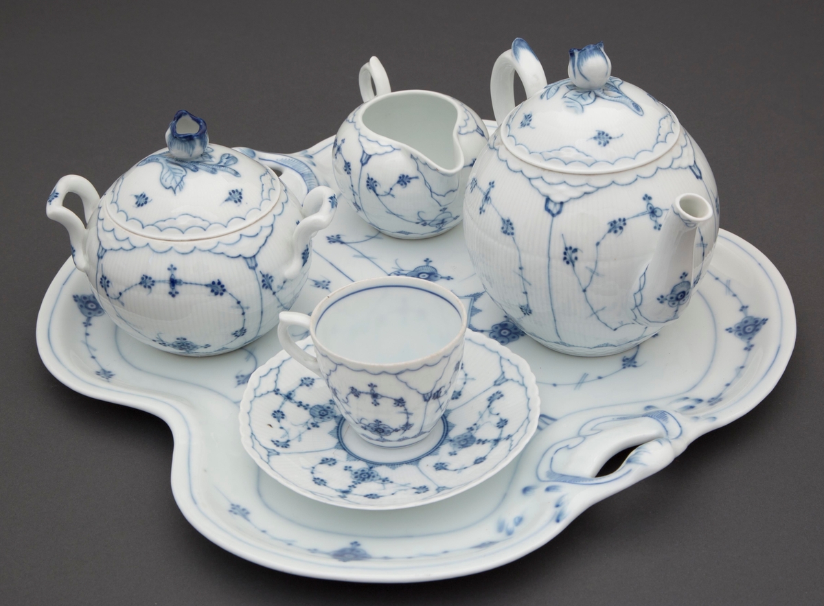 Kopp med skål i glasert porselen, dekorert med koboltblå underglasurmaling i form av stråmønster. Vertikale riller på koppen, mens skålen har radiære riller.