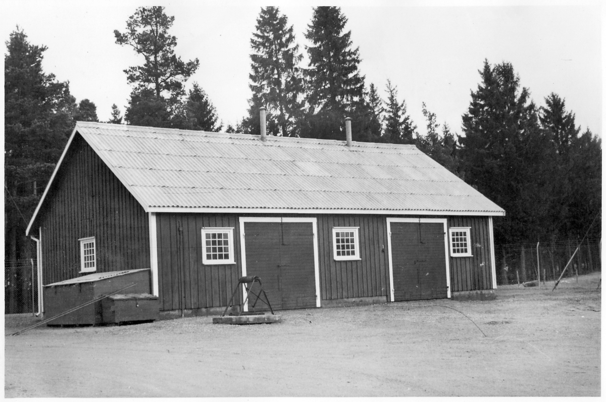 Vägstation P9, Ljung. Förrådsbyggnad (äldre garagebyggnad). Brunn med vinsch framför byggnaden. På gaveln redskapslådor.