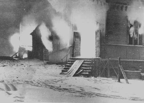 Det er vinter og sne i bakken med fotspor i. Flammer slår ut av vinduer på trebebyggelsen in Hammerfest. Bildet viser Folkets hus som ble tent på av tyske soldater i høsten 1944 i likhet med resten av byen.
