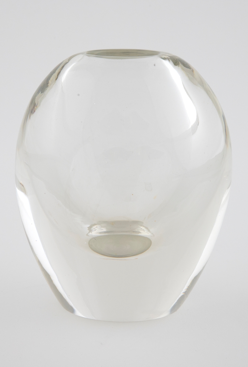 Ovalformet vase i tykt, klart glass med liten sirkulær åpning.