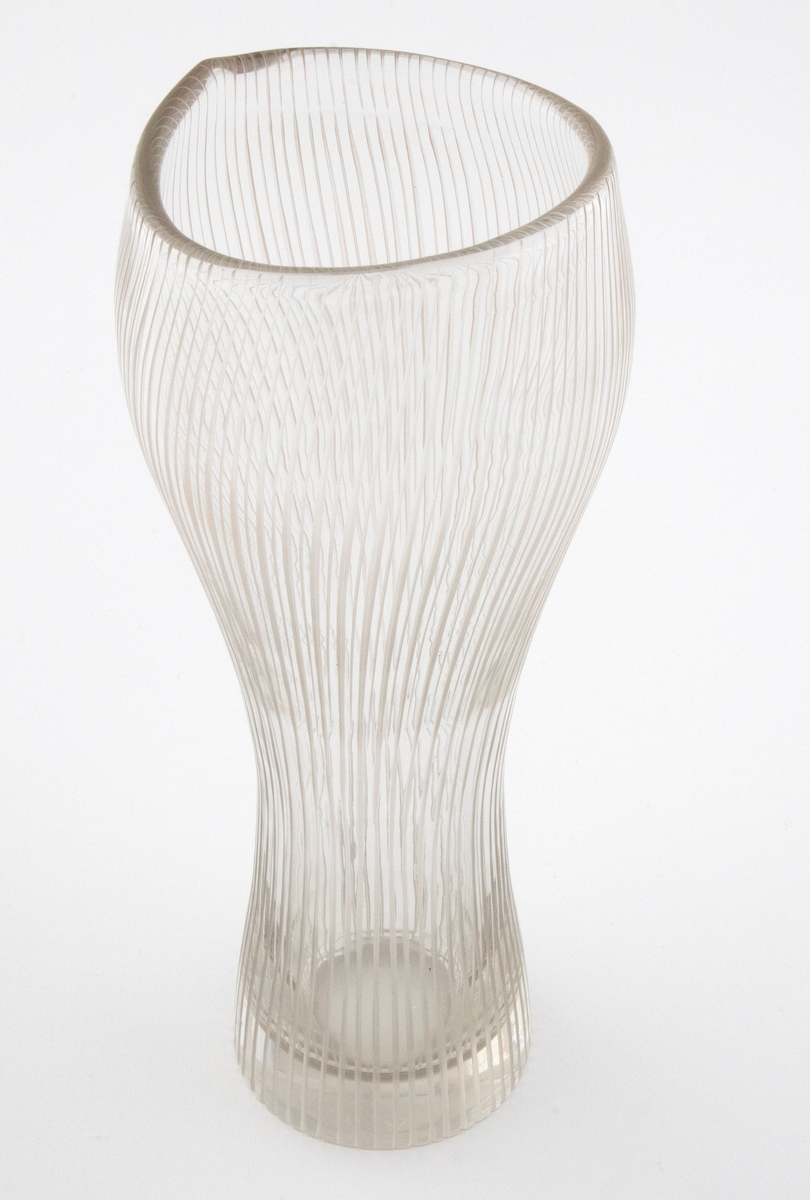 Høyreist vase i klart glass. Uregelmessig, bølgende munningskant. Korpus er dekorert med hjulgravering i form av spiralformede, vertikale linjer; dobbelt så mange linjer på over- som på underdelen.