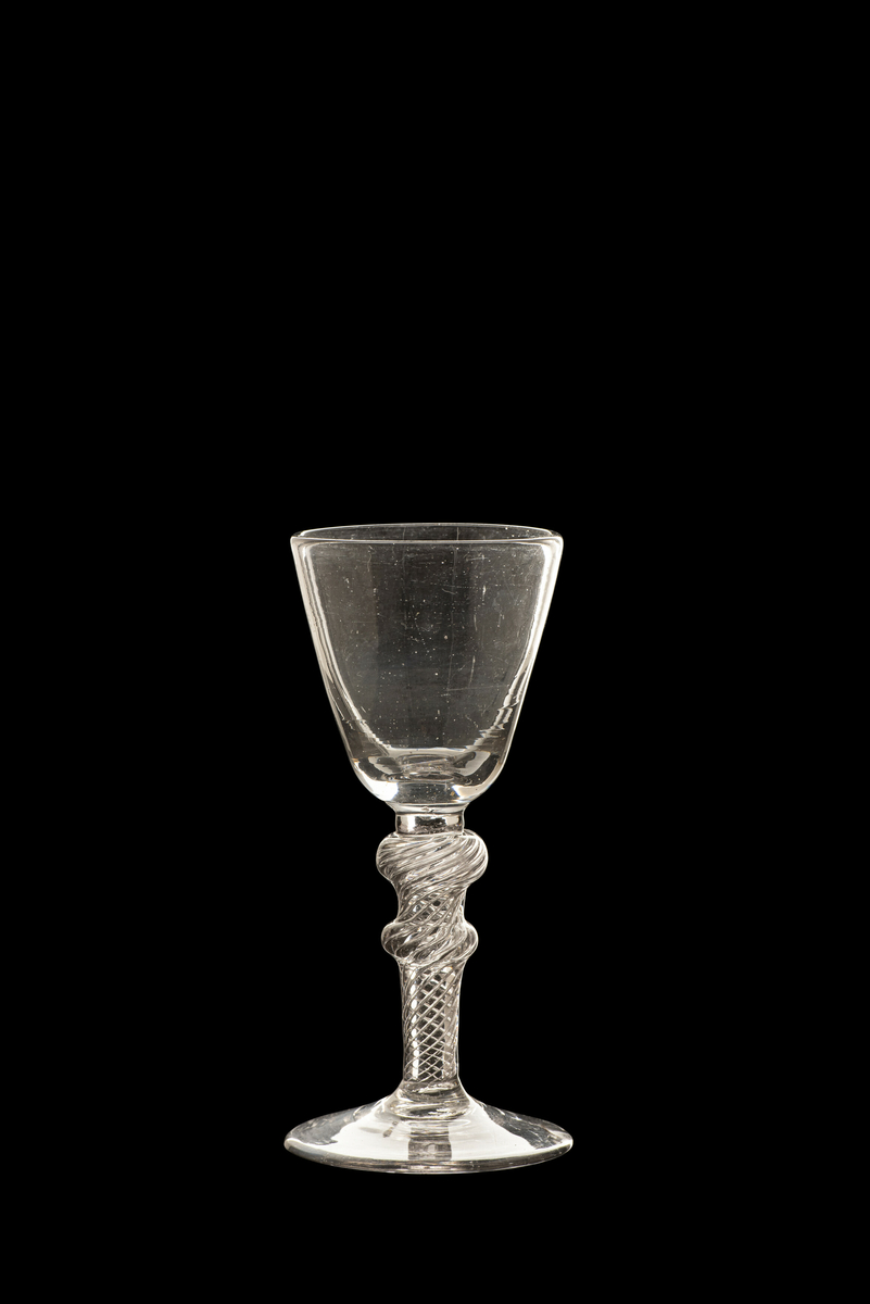 Dessertvinglass, modell "Desert Chrÿstal". Lett grålig, klart glass. Konisk klokke, på stett med vridde luftspiraler og to vulster. Nøstetangen eller Hurdal glassverk. Antagelig 1770-årene.