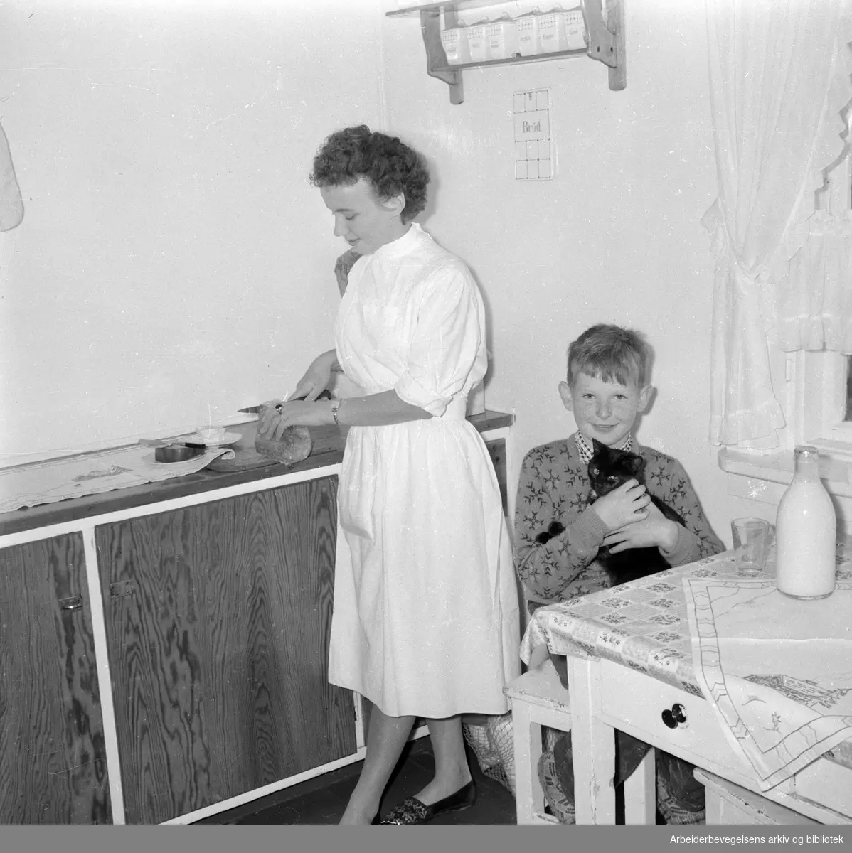 Husmorvikar Borghild Pedersen hjelper Tor Harald Smestad med matpakka. Nes på Romerike, september 1957.