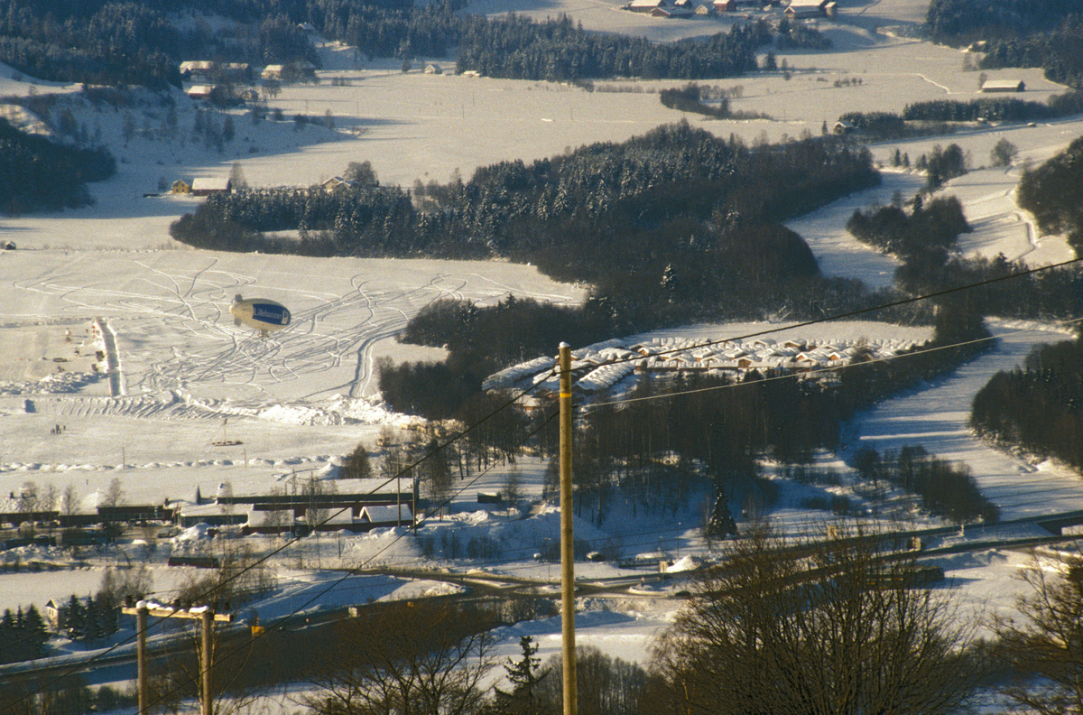 Lillehammer.  Medialandsbyen på Langøya ses til høyre for midten av bildet.  CBS's luftskip ses til venstre for midten av bildet.  Del av midlertidig helikopterlandingsplass i venstre billedkant.  Gausa til høyre.  Gausdalsvegen med krysset med Jørstadmovegen nederst på bildet.  Utsikt mot vest fra nedenfor Balberg gård.