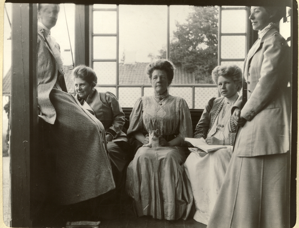 Fem kvinner, blant dem Nini Egeberg, Lucy Parr Egeberg og Hagar Parr på verandaen til Strøm (Vestre Strøm gård i Rælingen?). Fotografert juli 1909.