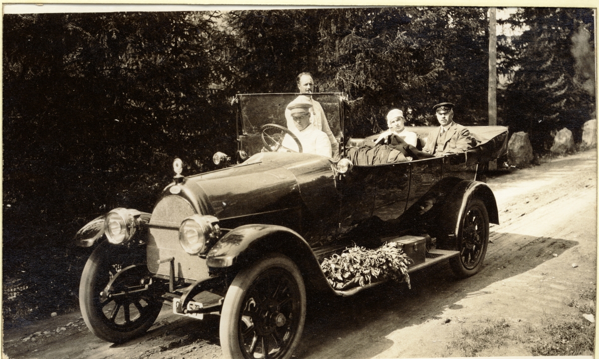 Egeberg-familiens sjåfør Kristian Skuggen kjører, i en Fiat, Waldemar Kallevig , Evelyn Egeberg og Westye P. Egeberg fra Lærdal etter fiske i Lærdalselvi. Laksen ligger i løv på trinnbrettet i tillegg til et reiseskrinn. Fotografert sommeren 1916.