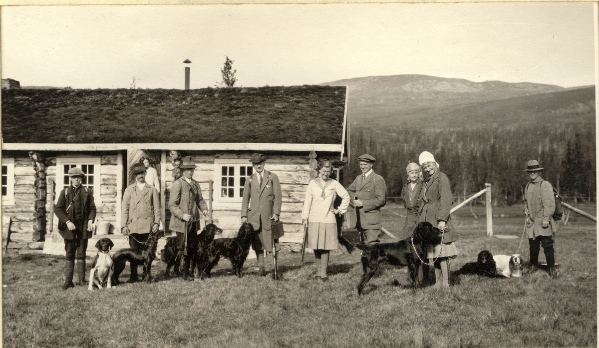 Jaktlag med hunder foran Fearnley-familiens jakthytte ved Øst-Fjerpen i Meråker. Fra venstre tre hjelpere, Nils O.Y. Fearnley, Ellen og Carlos Jakhelln, to ukjente, Vera Kallevig og en hjelper. Fotografert 1916.