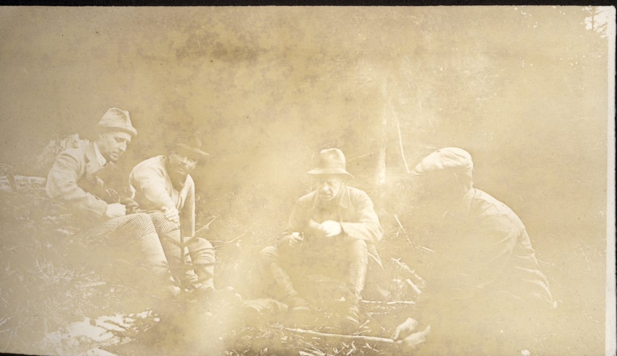 Fire menn tenner bål i skogen, antagelig ved Malungen i Hedmark. Blant mennene er antagelig Søren Sommerfelt, Fritz Treschow og Adolf Eger. Hunden "Siri" fra Bogstad skimtes på fanget til venstre.Fotografert oktober 1922.