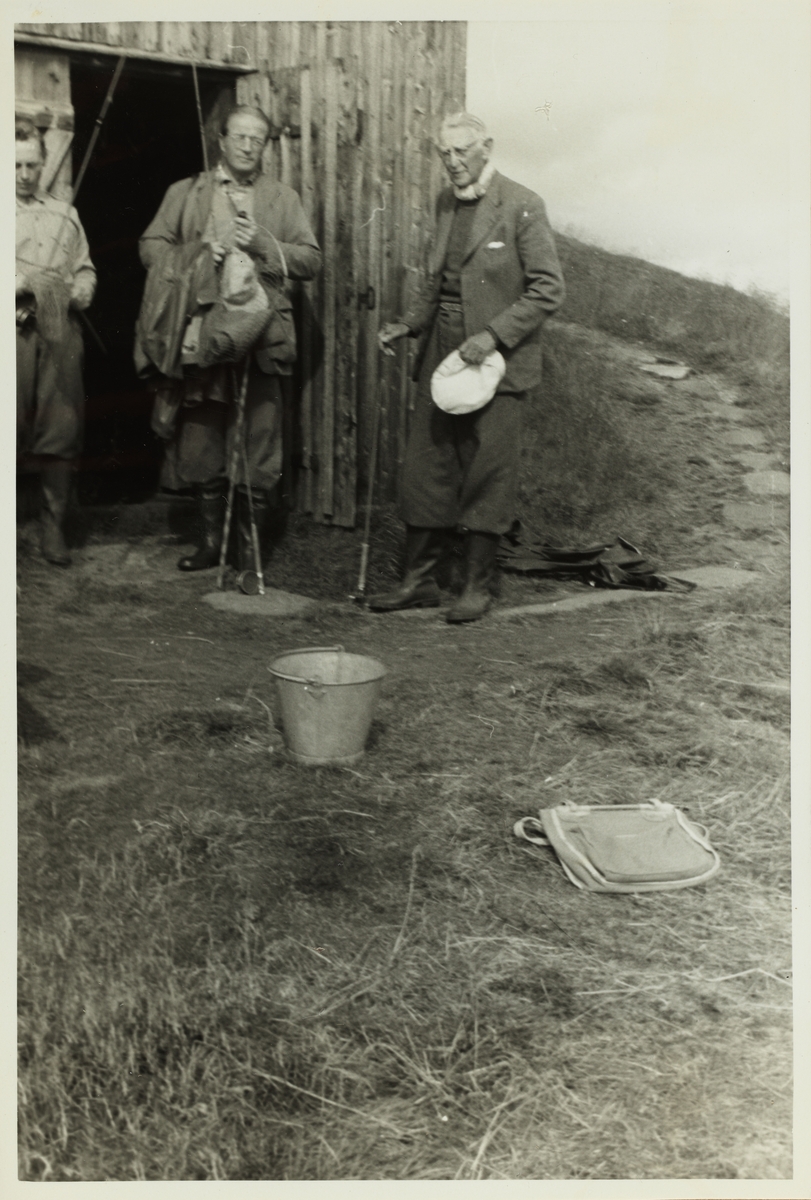 Carl Otto Løvenskiold og Aksel Hansen med fiskeutstyr utenfor fiskebu. Ukjent mann til venstre. Fotografert 1953.