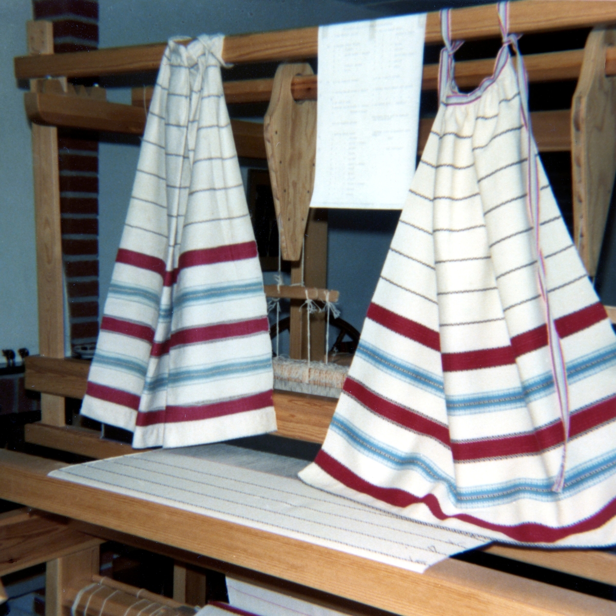 Kållereds Hembygdsgille, 1980-tal. Förlagor, som hänger i en vävstol, till Kållereds Hembygdsdräkt från Sporred. Till vänster ses förlagan till förkläde och till höger en uppvävd kopia.