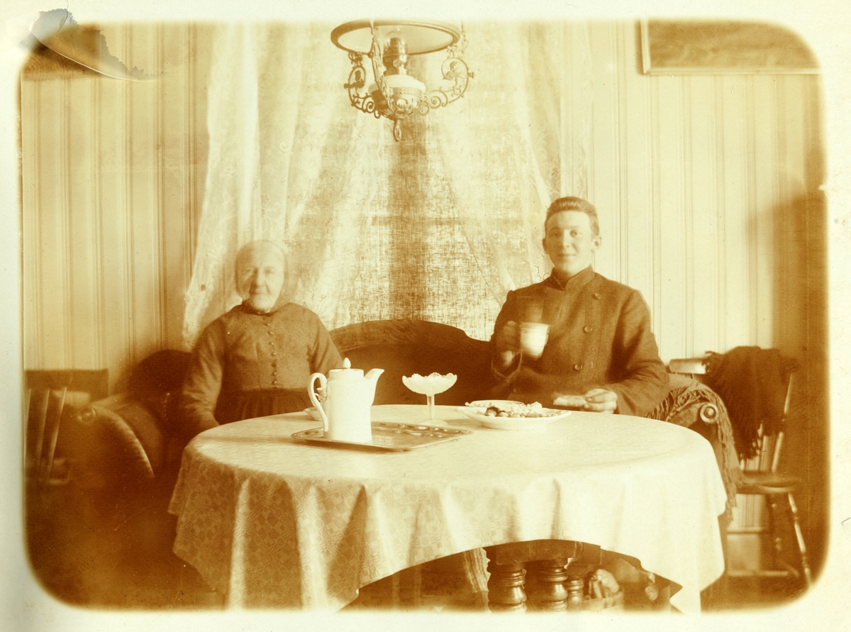 Interiørbilde fra gartnerboligen på Bygdø Kongsgård. To ukjente personer ved kaffebord med kaker.