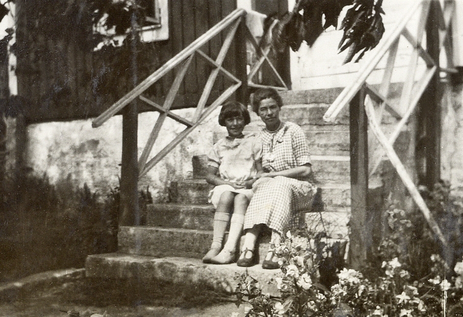 En kvinna och en flicka sitter på en trappa till ett bostadshus. 
Under fotot text: "Hällevik, 1929".