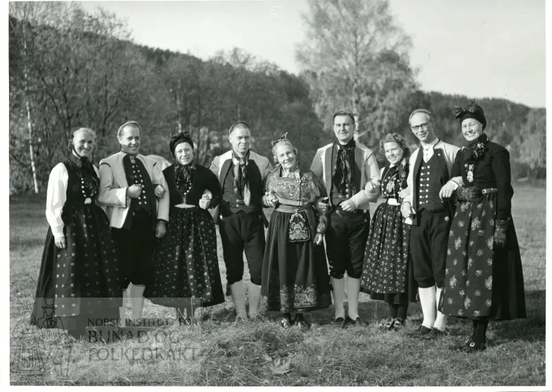 Gruppebilde med kvinner og menn i bunad. Leikarringen på Kongsberg i Numedalsbunader, Klara Semb i Telemarksbunad i midten.
