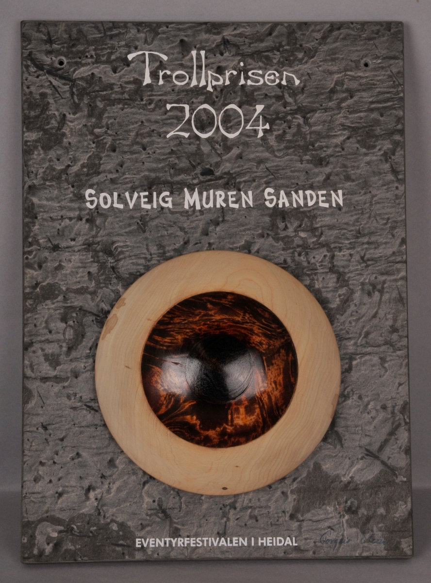 Steinplate med eit stort auge, og teksten "Trollprisen 2004 Solveig Muren Sanden Eventyrfestivalen i Heidal".