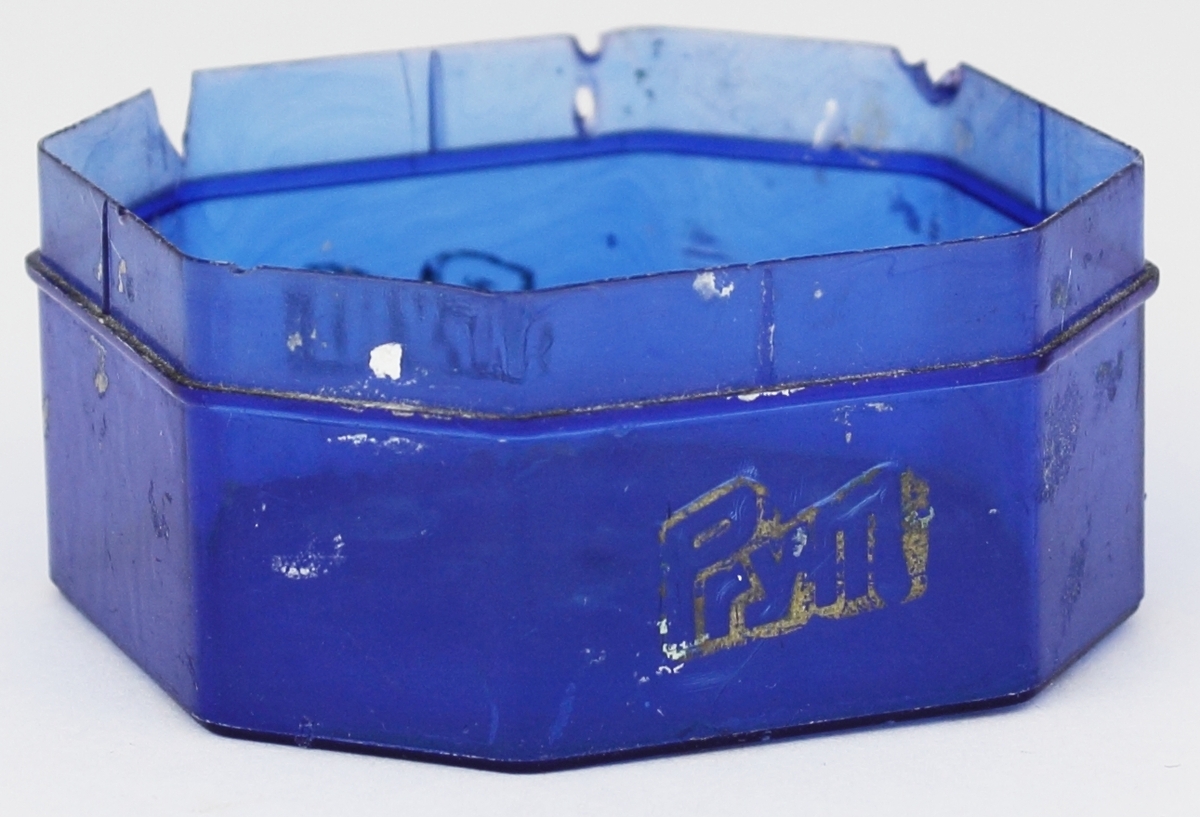 Åttkantig plastask i blå färg. På ena sidan finns text påtryckt. I asken har silvergranulater förvarats.