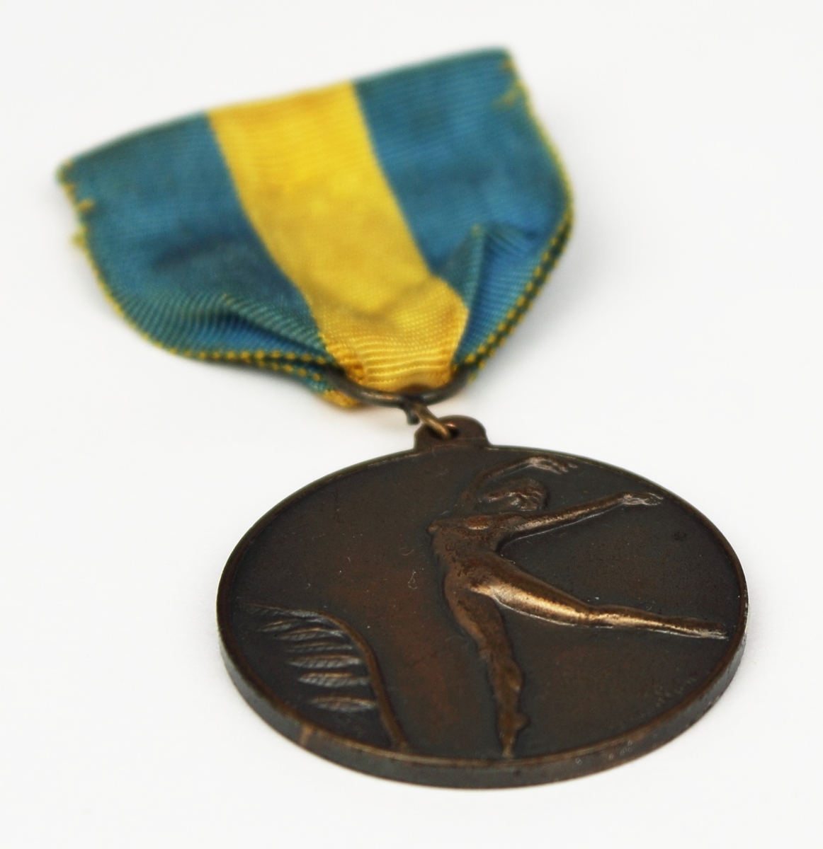 Medalj i brons fäst på blågult band. Medaljen har rund form med en naken kvinna i relief på framsidan.
