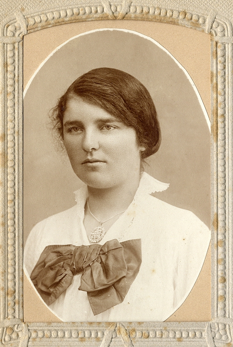 En ung kvinna i ljus blus med ståkrage och stor, mörk rosett. 
Bröstbild, halvprofil.