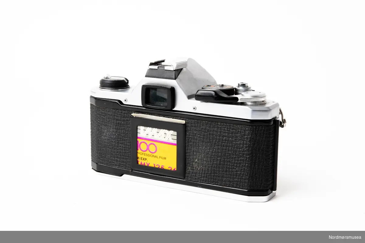 Pentax MX 35mm speilreflekskamera. Produsert i perioden 1976 -1984. Har et 28mm objektiv. Medfølger originalt skinnetui og deksel til objektivet. Påskrevet med rød tusj, iformasjon vedrørende bruk av blitz på dette kameraet. Inne i etuiet er det påklistret en merkelapp med NORDMØRE MUSEUM påskrevet.