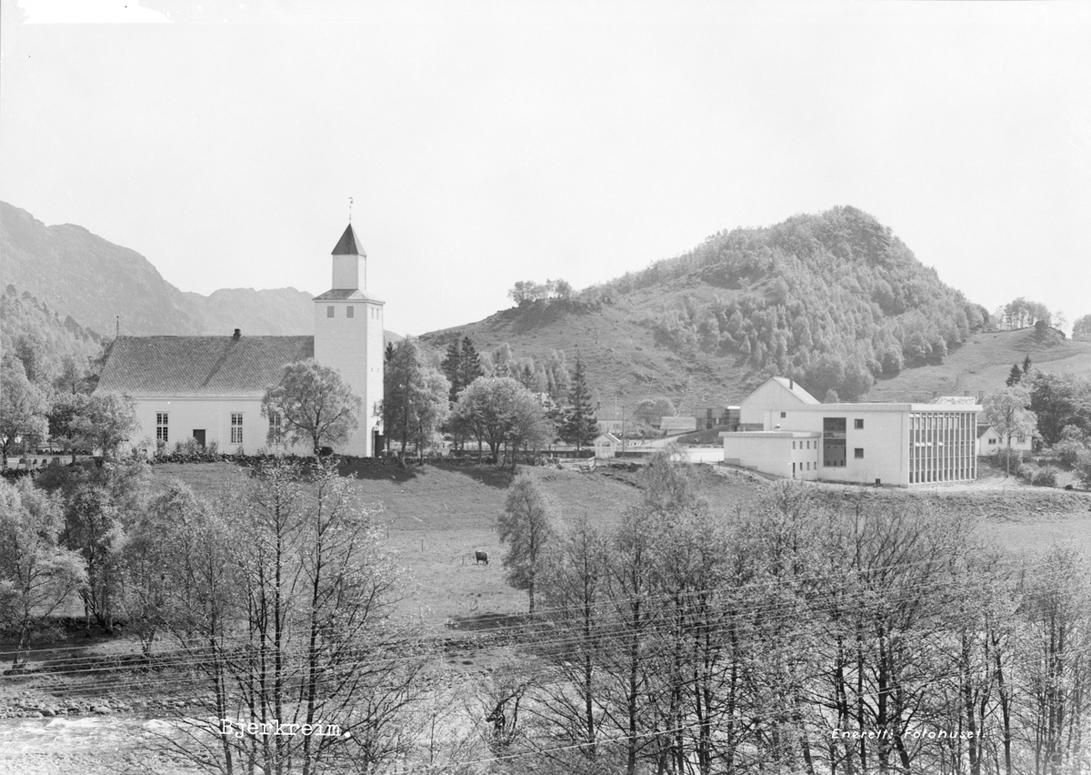 Bjerkreim kirke med Bjerkreim skule til høyre. I forgrunnen renner Bjerkreimselva og i bakgrunnen ligger Mæråsen. Nederst på det første bildet står det "Bjerkreim" og Enerett: Fotohuset."