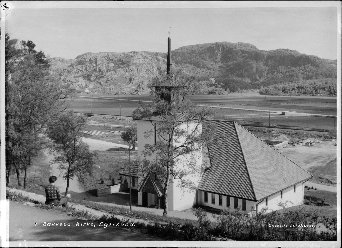 En person sitter i bakken ovenfor Bakkebø kirke i Egersund og ser utover.