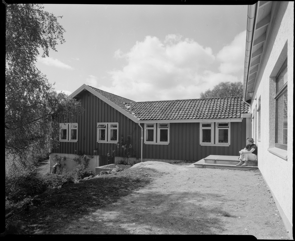 Bærumsgården på Bakkebø hjem og arbeidsskole. En kvinne sitter på trappeoppgangen.