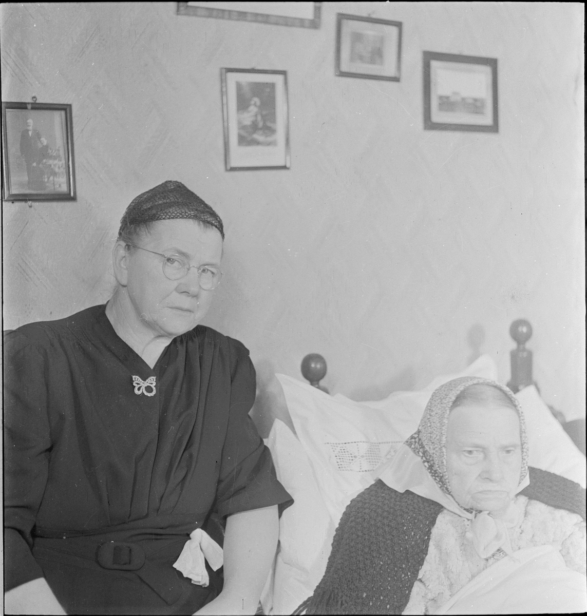 En kvinne sitter ved siden av en eldre sengeliggende kvinne.