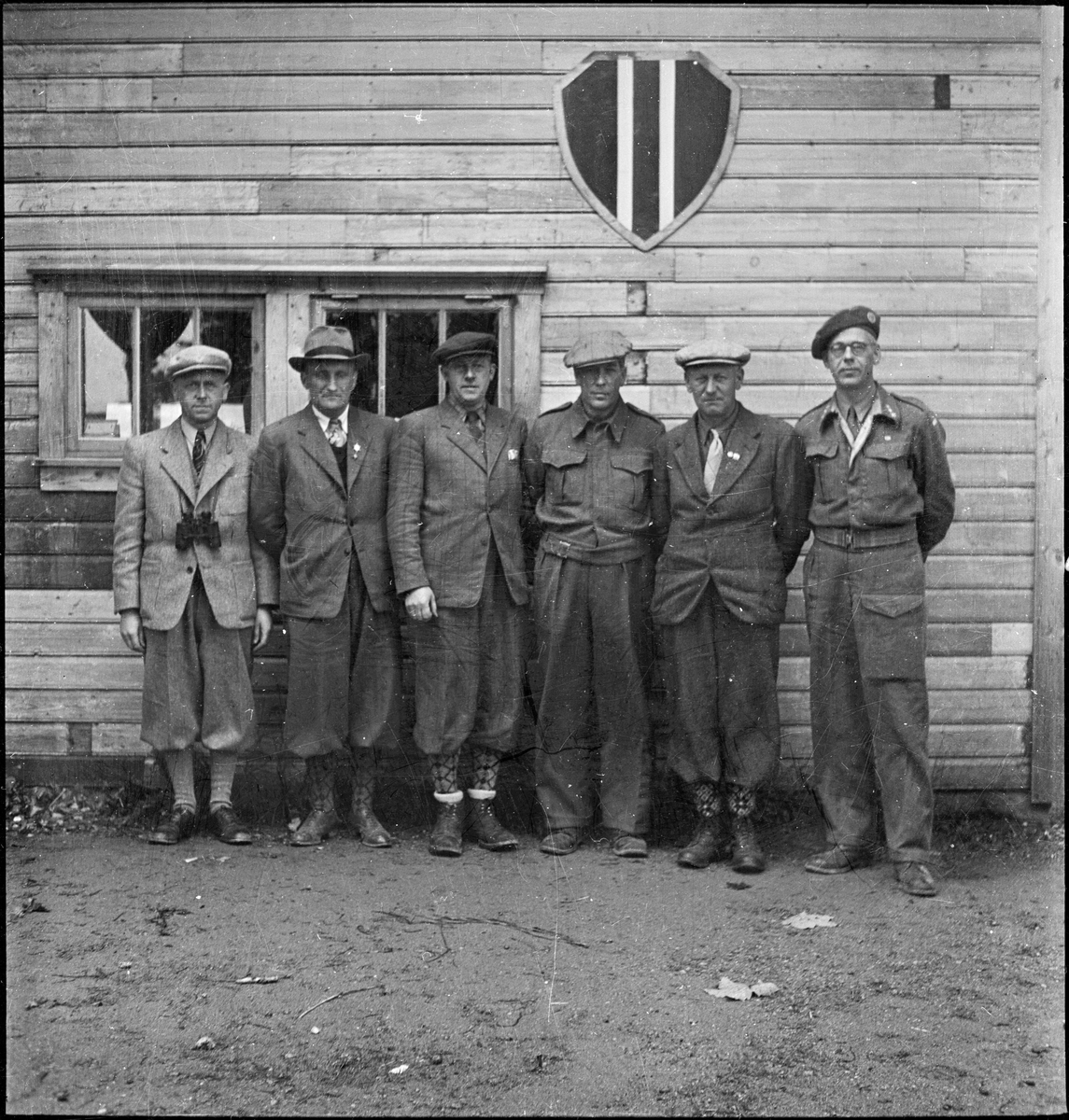 Seks menn står under logoen til Egersund skytterlag på Nyeveien. To har på militær- eller heimevernsuniform.