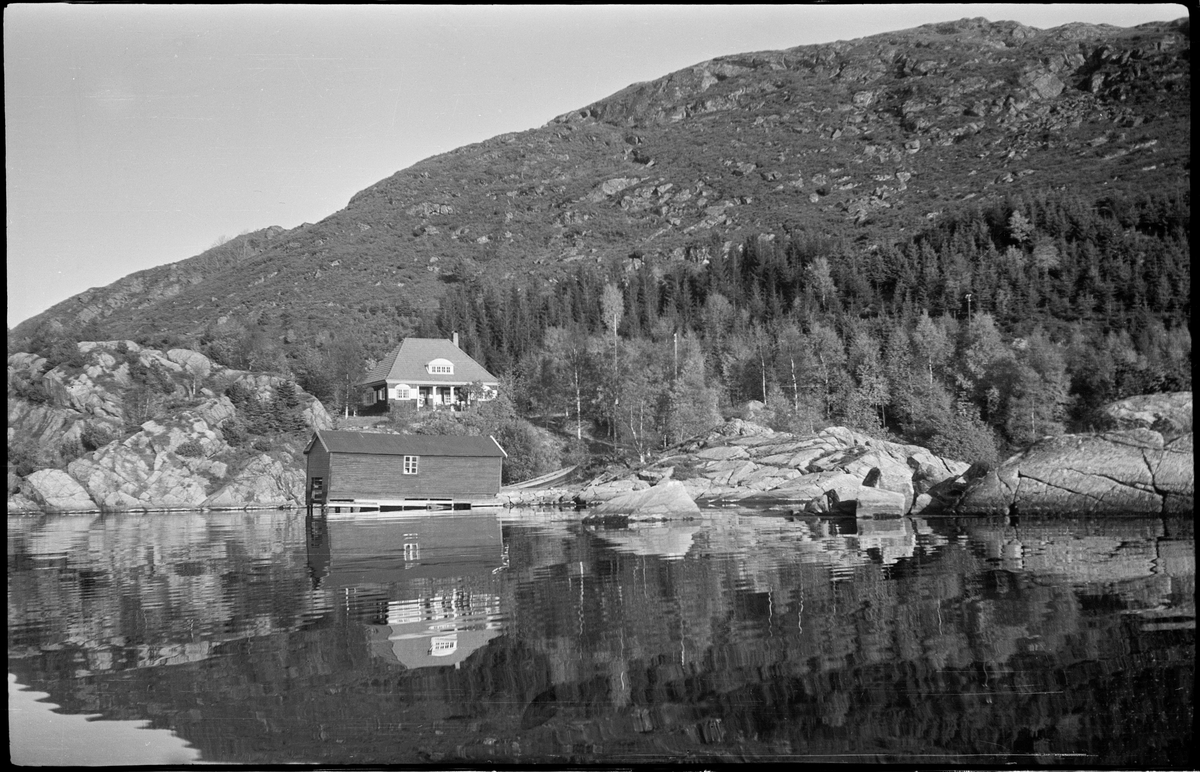Åsheim ved Søra Sundet i Eigersund. Det er en villa med et naust nede ved sundet. En åpen båt ligger bak naustet.