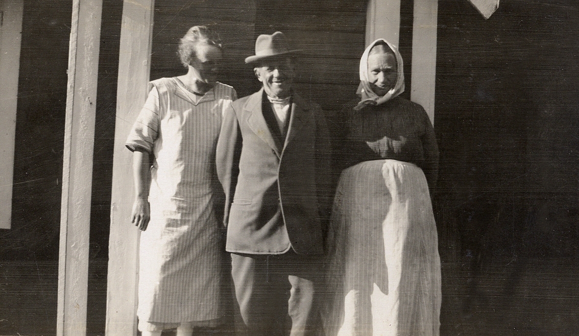 En yngre kvinna står tillsammans med ett äldre par utanför en stuga.