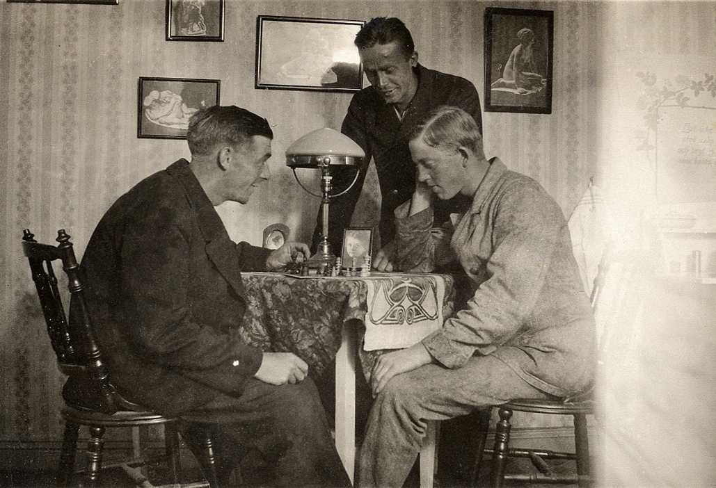Två unga män spelar schack, medan en tredje tittar på.