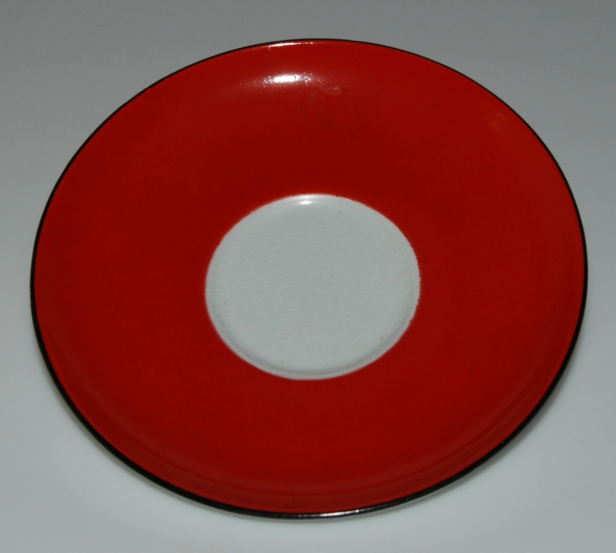 Tekopp med fat, röd glasyr med vita prickar samt två svarta linjer på insidan av koppens överkant. Okänd formgivare och dekoratör. Kan vara inspiration till den senare (1949-57) av Helmer Ringström skapade dekoren Amanita.
