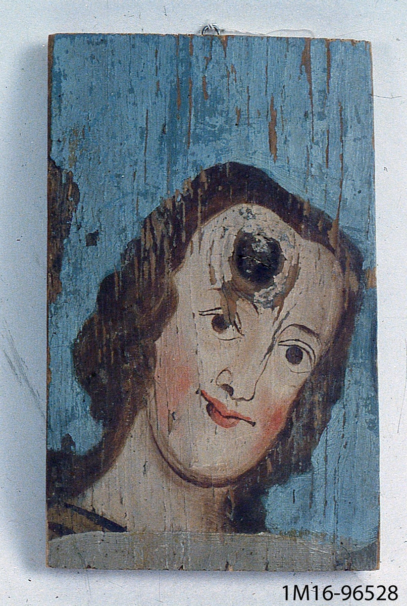 Oljemålning på trä. Kvinnoansikte med brunt hår mot blå bakgrund. Från Bjurbäcks gamla kyrka, nu riven. Senare placerad i fattighuset.