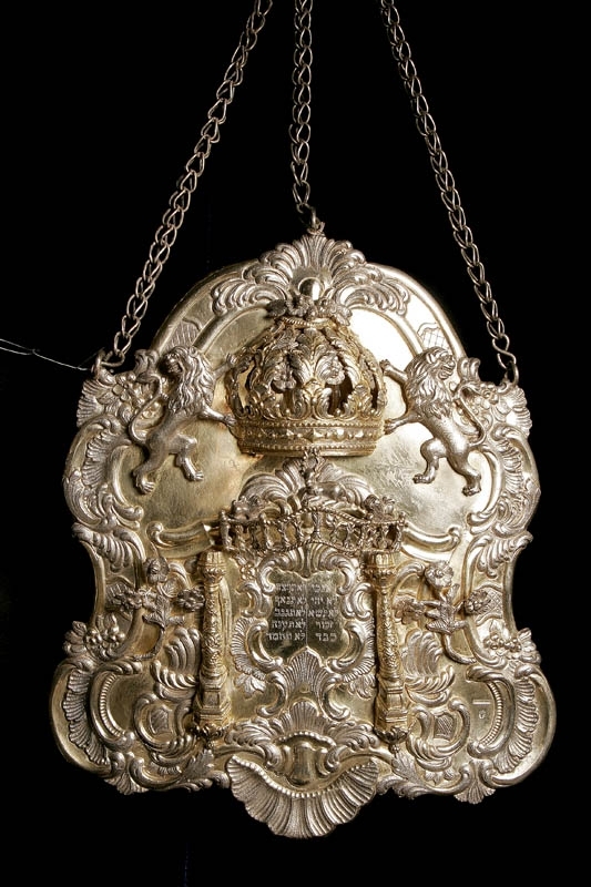 Torahsköld tillverkad av silver. Skölden är delvis förgylld och är rikligt dekorerad med en tredimensionell krona flankerad av lejon. Blommor och djur, samt ristad hebreisk text.