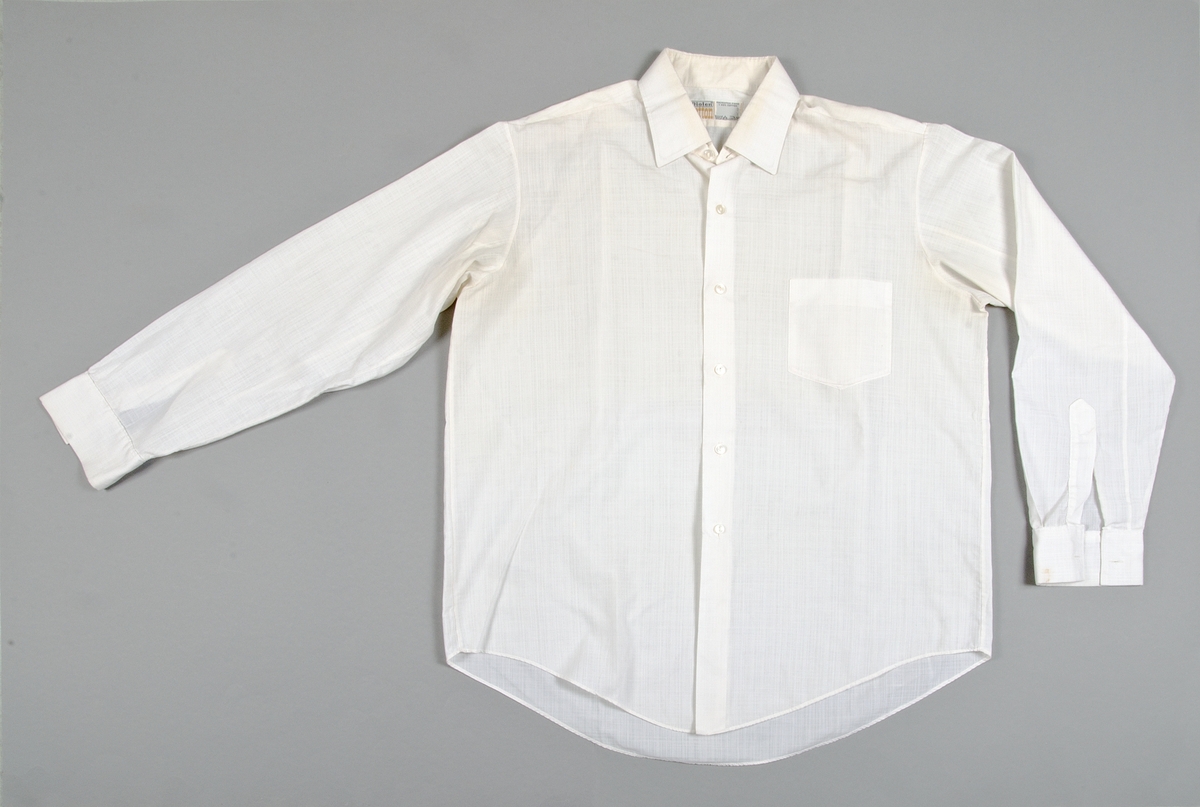 Skjorta av vit bomull och polyester. Långa ärmar. Bröstficka. Hål för manschettknappar. Märkt: Diolen COTTON, POLYESTER FIBRE + 33% COTTON.