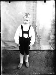 En liten gutt står i kortbukse med seler.