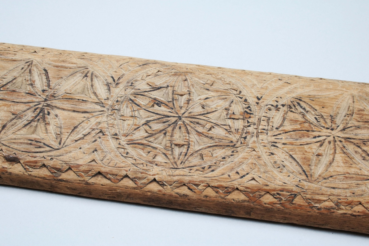 Mangelbräde i brunbetsat trä (färgslitage). På ena änden, infällt, skuret handtag (ej original). Brädet med skuren dekor, i form av 6 bladrosetter inom zig-zagbårder. Långsidor nedfasade. Närmast handtaget rektangulär ram med rutmönster. På ovansidan skuret: IAS ALO, 1747

Mangelbräde eller kavelbräde är ett redskap av trä som använts för mangling av textilier. Mangelbrädet användes tillsammans med en kavel, en slät rulle av trä. Den textil som skulle manglas, rullades upp på kaveln, på ett bord eller annat slätt underlag. Under hårt tryck, rullades kaveln med hjälp av mangelbrädet, fram och tillbaka över bordet. (Wikipedia)